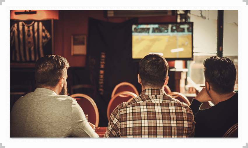 Three guys sitting at a bar watching TV